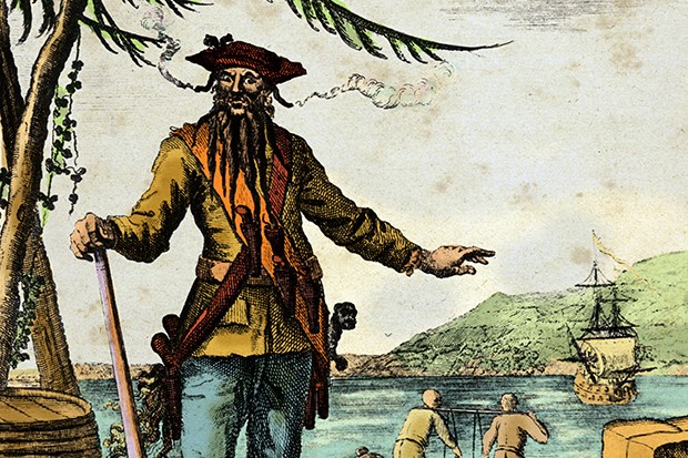 Blackbeard, real name Edward Teach, seen standing on a dock with fuses in his beard